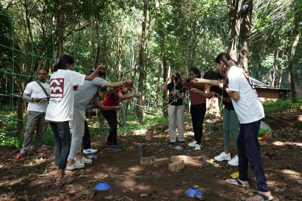 Participants wearing AEL T-shirts are actively engaged in a team-building activity in an outdoor setting. They are collaborating, communicating, and having fun as they complete the challenge together.